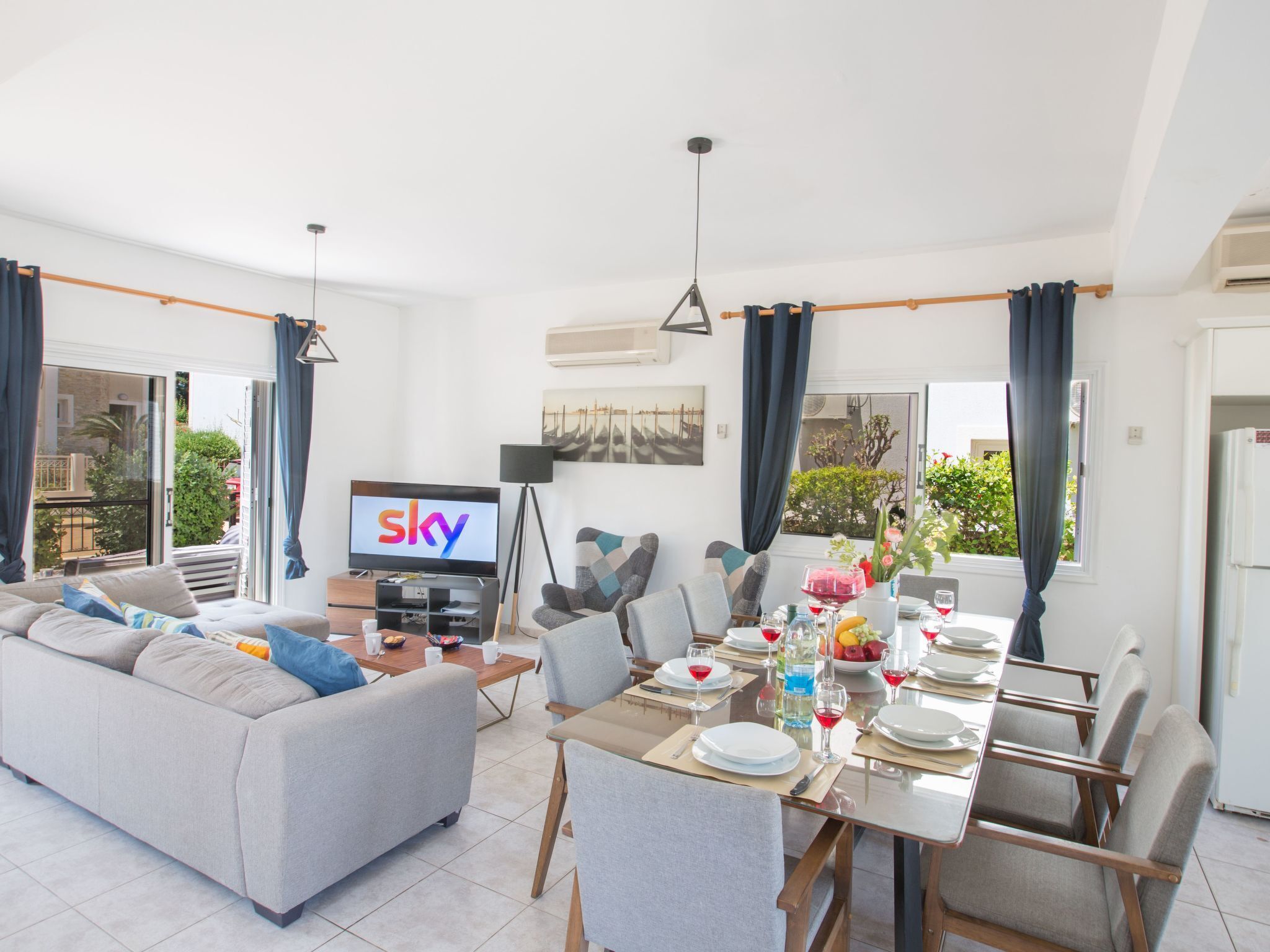 A modern living room with a sofa, dining table set for four, and a TV displaying 'sky'.