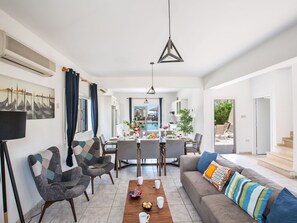 Ein modernes Wohnzimmer mit Essbereich, einer Couch, einem Couchtisch und Blick auf einen Pool.