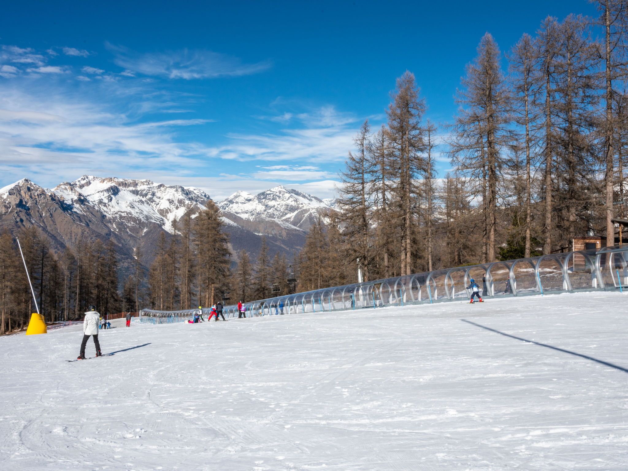 Una pista da sci innevata con cielo sereno e montagne sullo sfondo.
