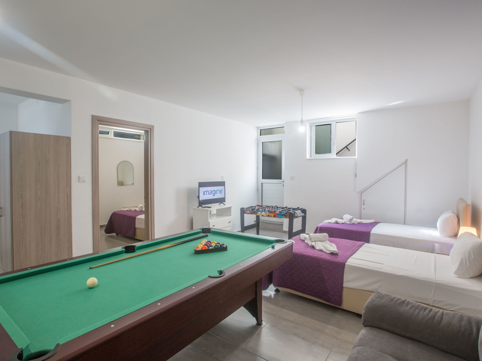 Een ruime kamer met een pooltafel, een bank, een bed en een televisie.