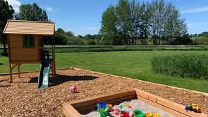 A playground with a wooden playhouse, a slide, and a sandbox filled with toys. - Appartement mit Balkon by Interhome (Baabe)
