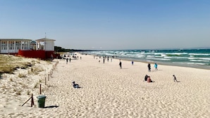 A wide sandy beach with a few people and a building with a red roof and white walls. - Appartement mit Balkon by Interhome (Baabe)