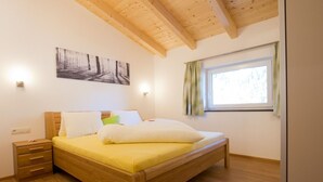 Une chambre à coucher avec un lit en bois, une table de chevet, une fenêtre avec des rideaux et un tableau au mur.