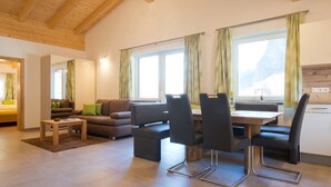 Un salon moderne avec un plafond en bois, un ensemble de canapés, une table à manger avec des chaises et de grandes fenêtres dotées de rideaux.