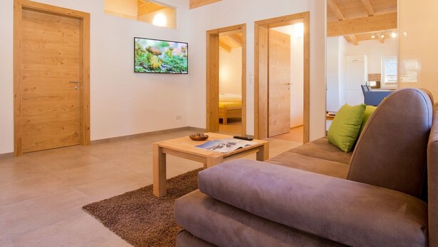 Un salon moderne avec un plafond en bois, un canapé, une table basse et un téléviseur fixé au mur.