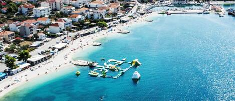 An aerial view of a coastal town with a marina, clear blue waters, and densely packed buildings.