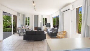 Un vaste espace de vie comprenant un canapé, une table à manger et des chaises, de grandes fenêtres et un appareil de climatisation.