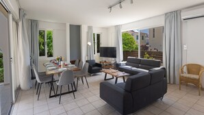 Un salon moderne avec un canapé, une table à manger et des chaises. On y trouve également un téléviseur et une fenêtre avec des rideaux.