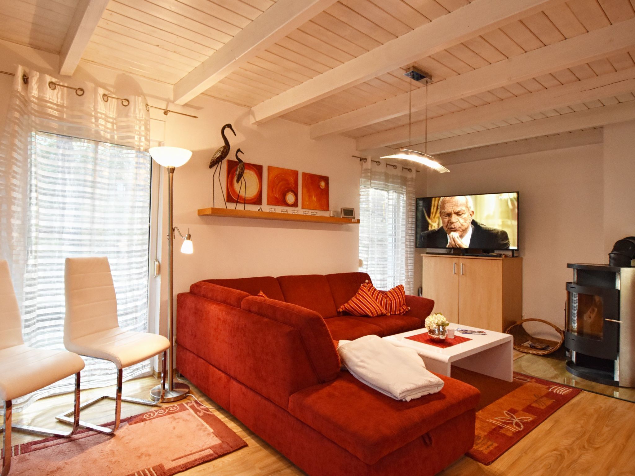 A living room with a red sofa, white armchairs, a TV, and a fireplace.