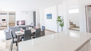 Een moderne woonkamer met een eethoek, een flatscreen-televisie en een groot raam met uitzicht op zee.