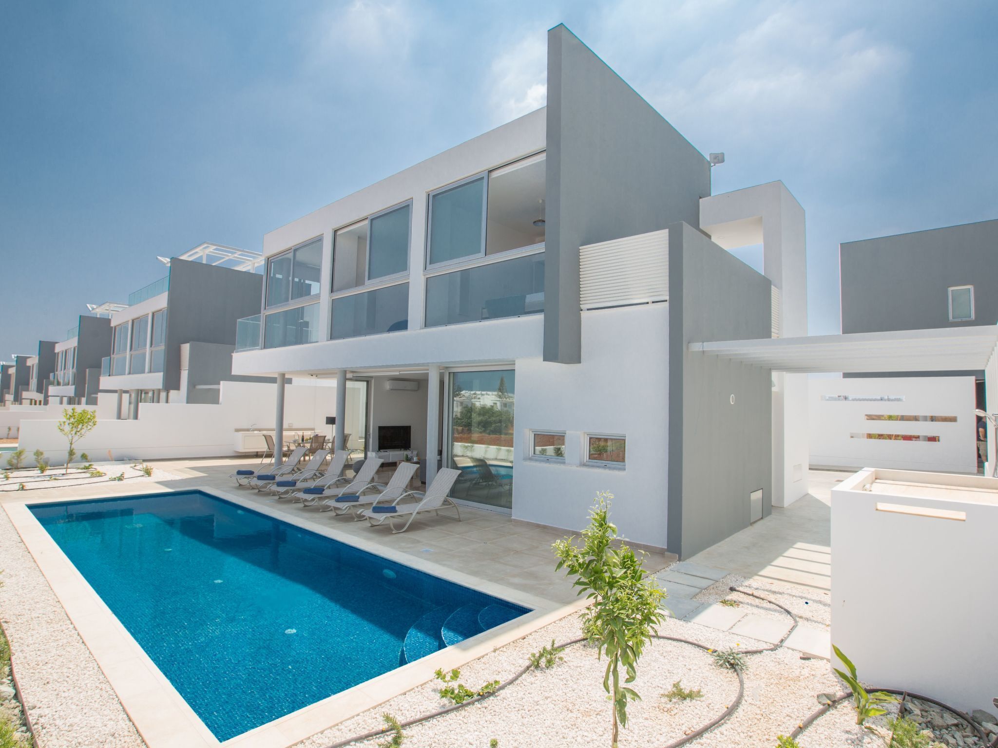A modern multi-story residential building with a swimming pool and sun loungers.