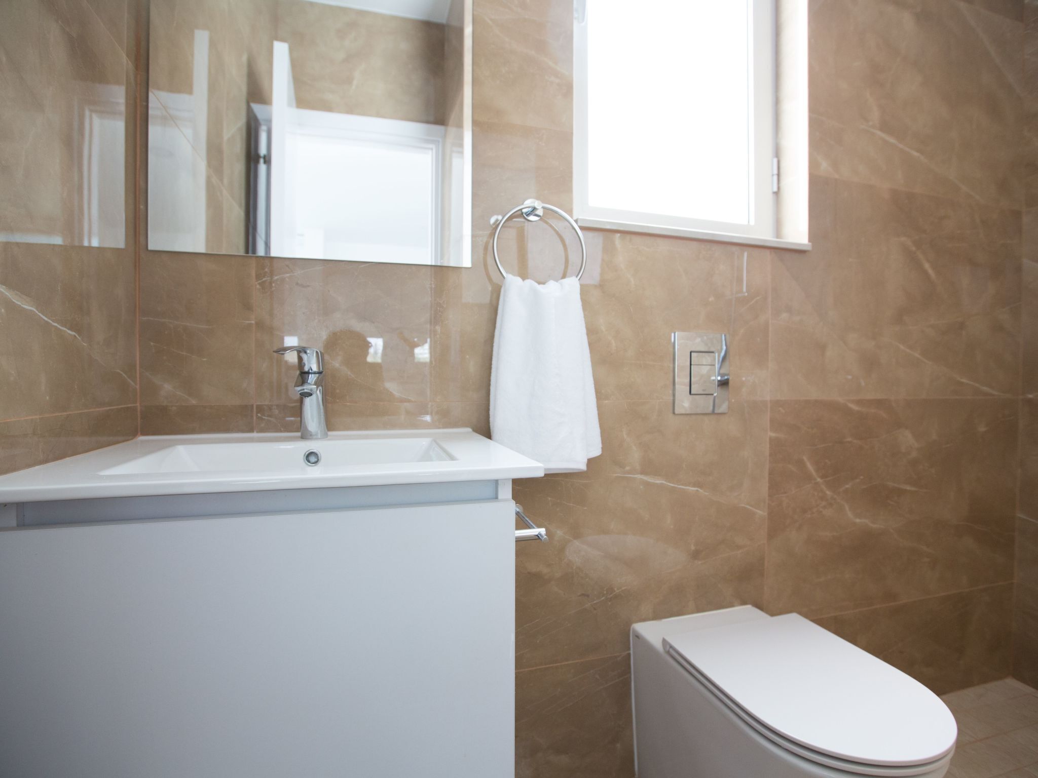 Un baño moderno con lavamanos, espejo y retrete blancos.