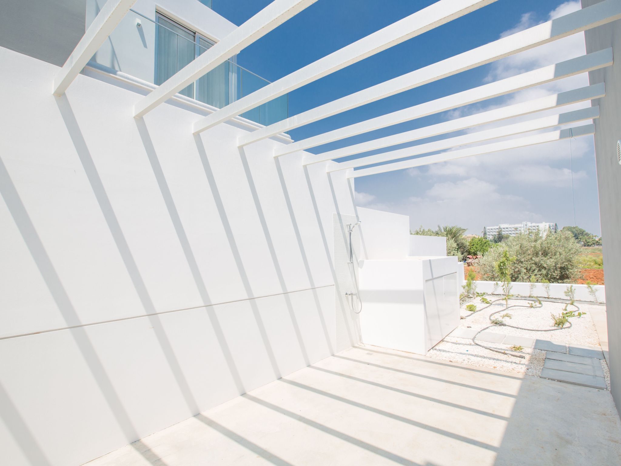 Un espace intérieur moderne et lumineux, aux murs blancs, offrant une vue dégagée sur l’extérieur, avec une structure de plafond géométrique et un jardin extérieur visible.