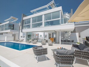 Une maison moderne à deux étages dotée d’une piscine, d’un espace extérieur aménagé et d’un coin repas.