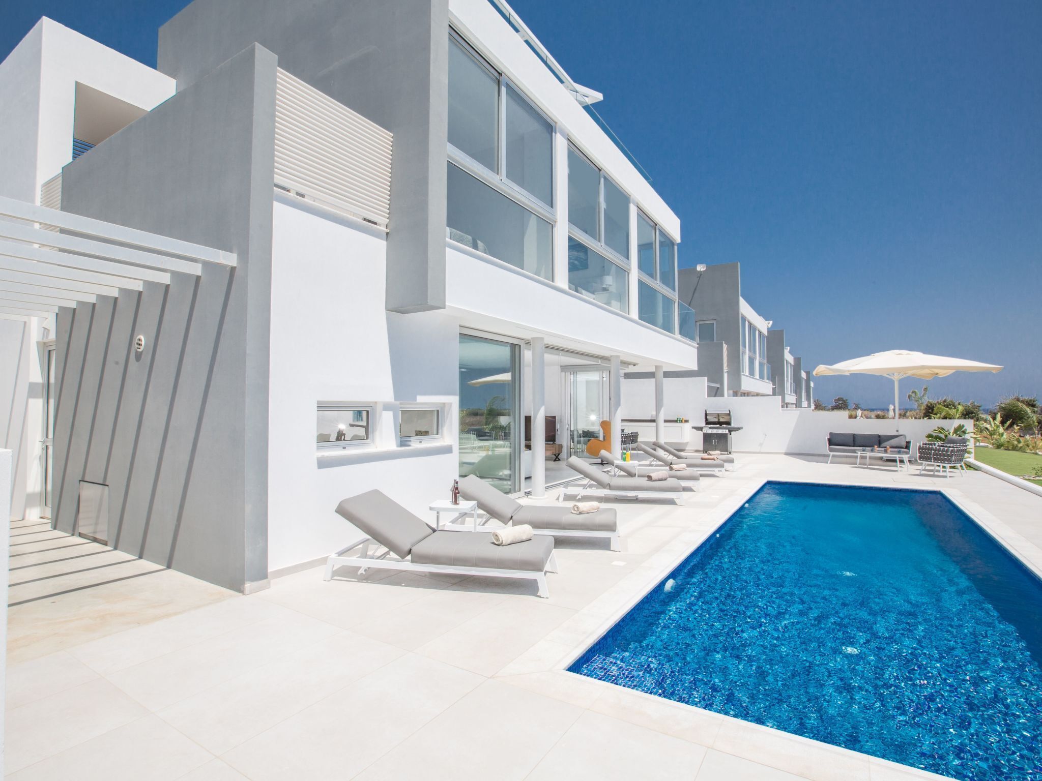 A modern two-story house with a swimming pool, sun loungers, and outdoor furniture.