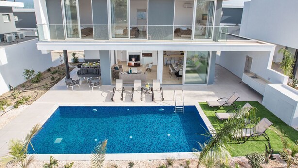 Ett modernt hus i två våningar med en swimmingpool, en uteplats och en stor glasdörr som leder in till huset.