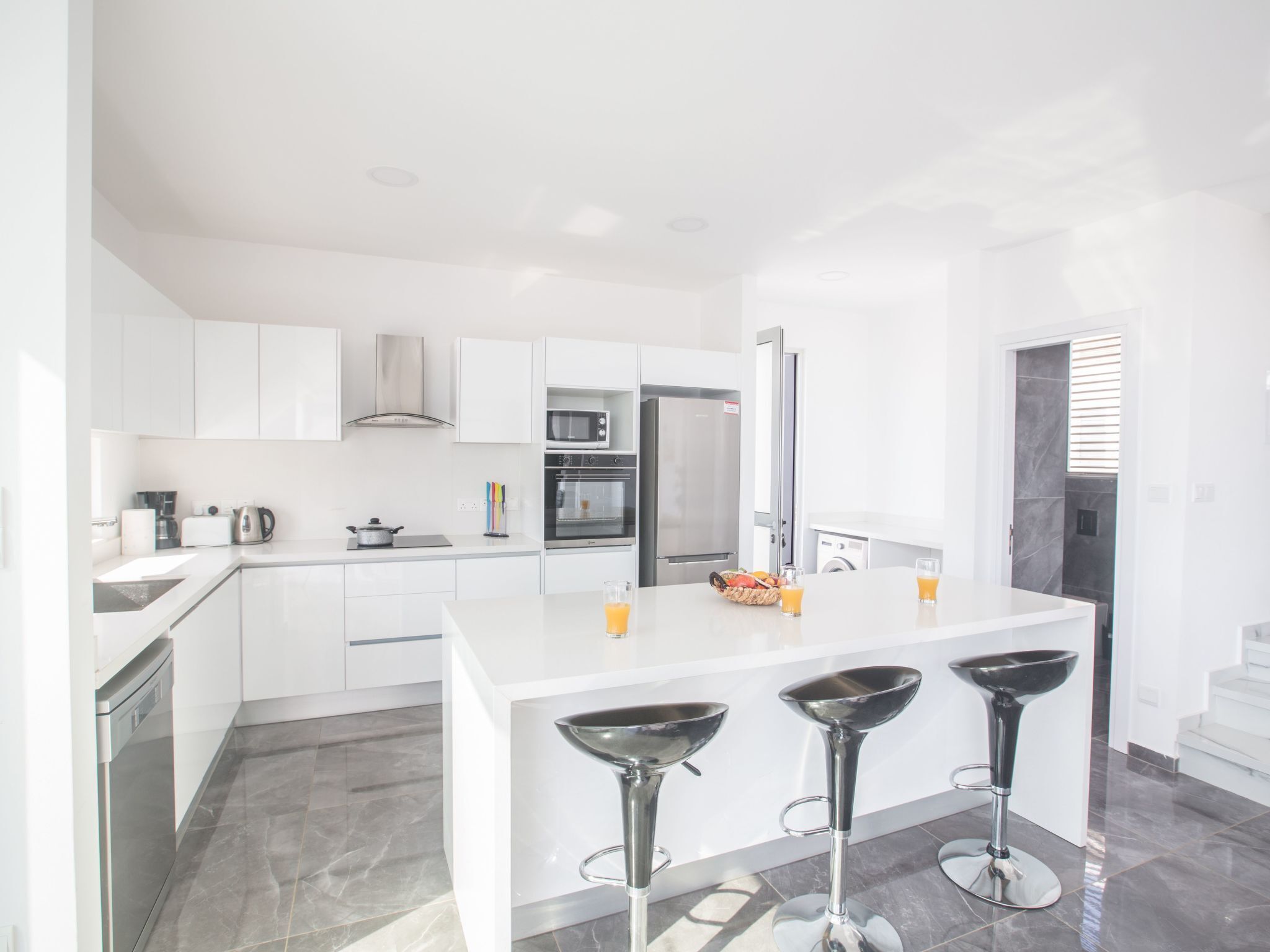 Een moderne keuken met witte kasten, roestvrijstalen apparatuur en een centraal eiland met barkrukken.
