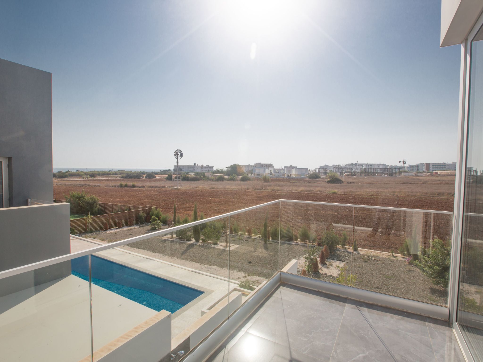 A balcony with a swimming pool, overlooking a barren landscape with wind turbines and distant buildings.