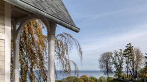 Ein weißes Gebäude mit Balkon, das auf einen angelegten Garten und ein Gewässer blickt.