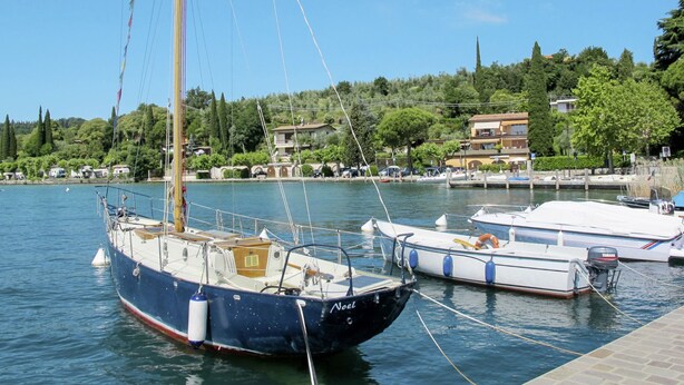 Un puerto deportivo con varias embarcaciones amarradas, cielo despejado y edificios al fondo.