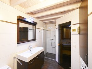 Ein modernes Badezimmer mit Waschbecken in Weiß, dunklen Holzschränken, einem großen Spiegel und einer Duschkabine aus Glas.