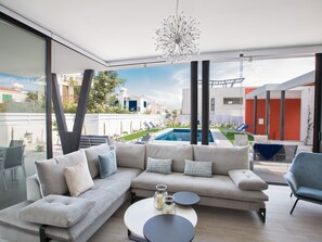 A modern living room with a sectional sofa, a coffee table, and a view of a swimming pool and outdoor area. - Neue, luxuriöse 3-Schlafzimmer-Villa in Protaras by Interhome (Protaras)