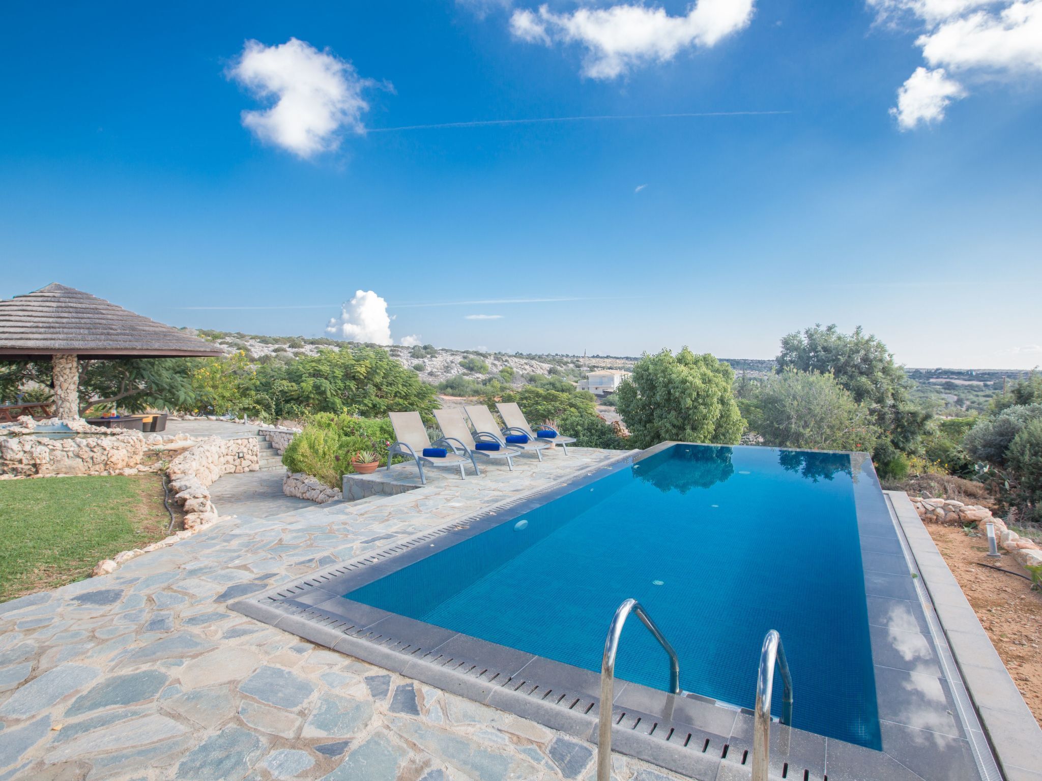 A rectangular pool with a stone deck, lounge chairs, and a gazebo.