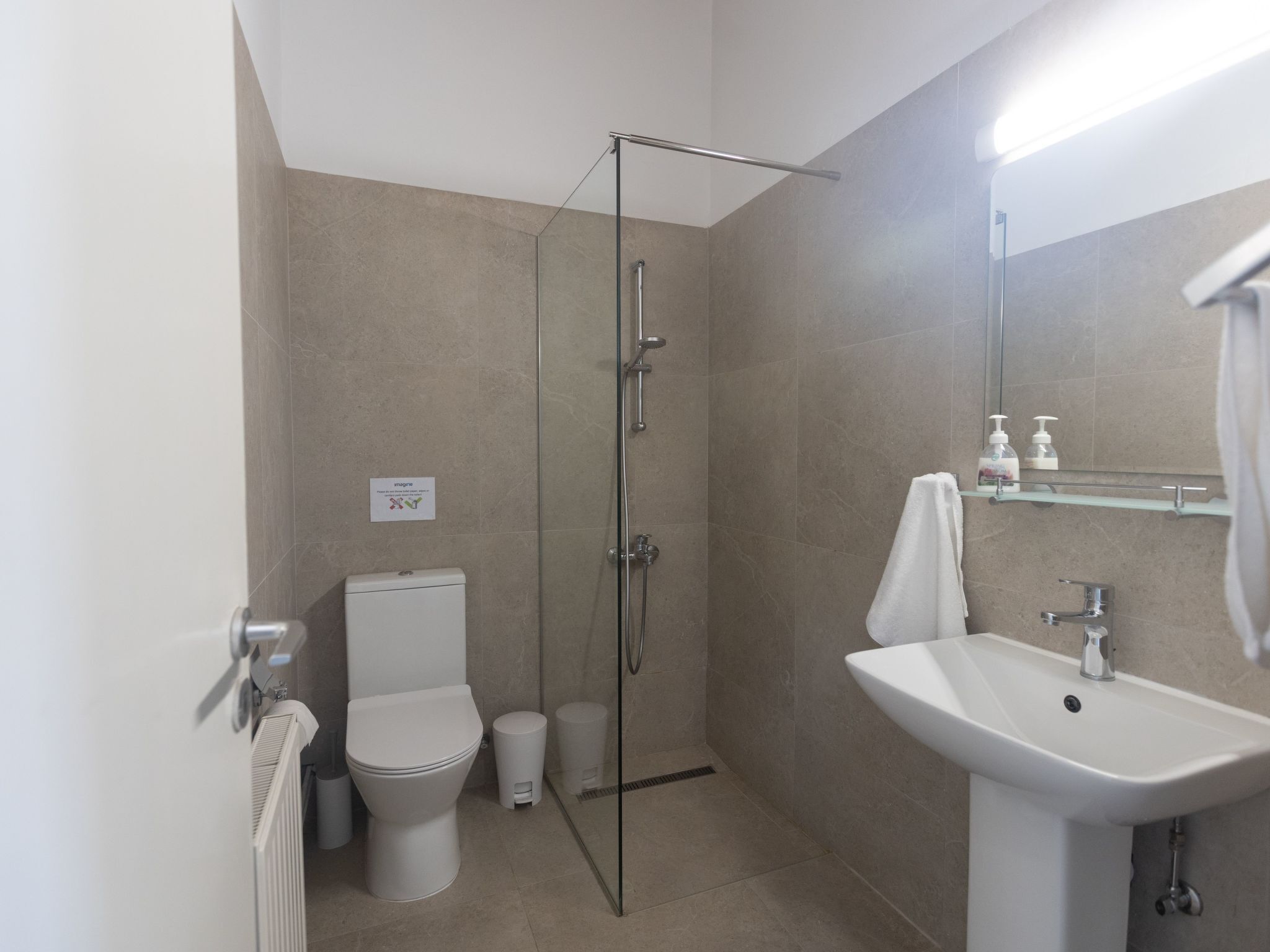 Een moderne badkamer met een douche met glazen wand, een wit toilet, een wastafel en een spiegel, met een handdoek aan de muur.