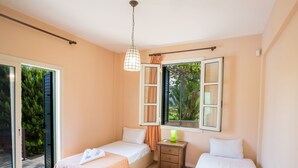Quarto com duas camas de solteiro, uma pequena mesa de cabeceira com abajur e uma janela com cortinas.