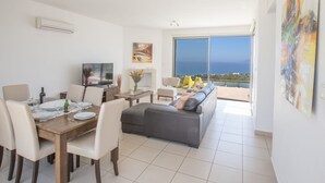 A modern living room with a dining area, a TV, and a large window with a view of the sea. - Villa mit Panoramablick auf das Meer von Latchi by Interhome (Polis Chrysochous)