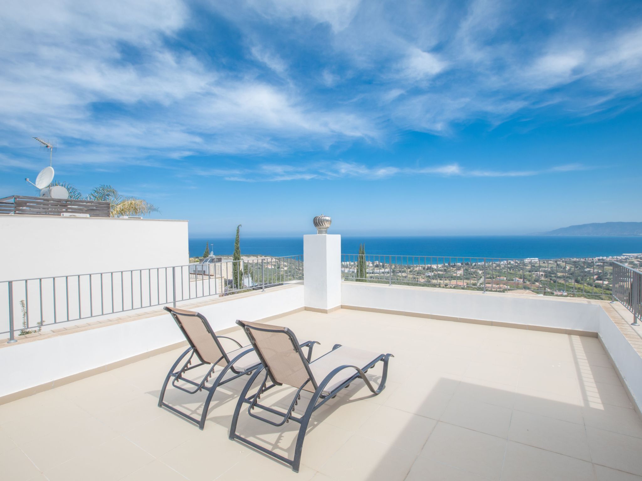 A rooftop terrace with two chairs and a table, overlooking a coastal cityscape and the sea.