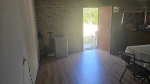Quarto com piso de madeira, uma pequena mesa com cadeiras, porta que dá para o exterior e aquecedor fixado na parede.