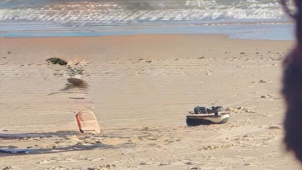 Uma praia com um barco e uma prancha de surf na areia.