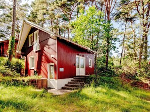 Eine rote Holzhütte mit geneigtem Dach, einer Haustür und einer kleinen Treppe, die zum Eingang führt.