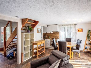 Ein modernes Wohnzimmer mit Sofa, Esstisch und Stühlen. Eine Treppe führt zu einer weiteren Ebene, es gibt eine Küchenzeile und ein großes Fenster mit Vorhängen.