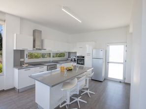 Una cocina moderna con armarios blancos, una isla central con taburetes y horno empotrado, además de un refrigerador.