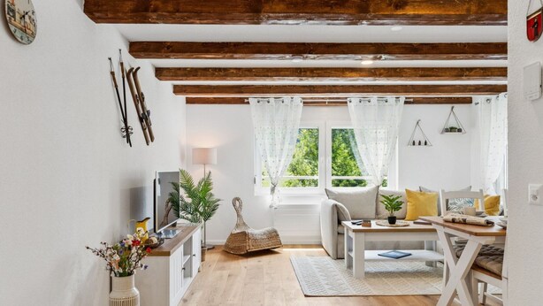 Ein gemütliches Wohnzimmer mit Holzbalkendecke, einer Couch, einem Esstisch und einem Fernseher.