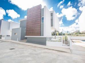 Ein modernes, zweistöckiges Haus mit flachem Dach, einer großen Holzverkleidung an der Vorderseite und einem weißen Zaun mit Tor.