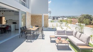 A modern outdoor living area with a dining table, chairs, and a sofa. There is a kitchen visible through an open door. - Protaras Vie Bleu Villa mit Pool, im Zentrum by Interhome (Protaras)