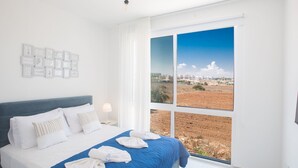 A bedroom with a large window, a bed with white and blue bedding, and a wall with framed pictures. - Protaras Vie Bleu Villa mit Pool, im Zentrum by Interhome (Protaras)