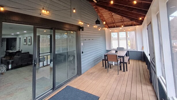 En overdækket terrasse med trægulv, et spisebord med stole og lyskæder.