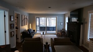 En moderne stue med sofa, lænestole, pejs og udsigt gennem store skydedøre.