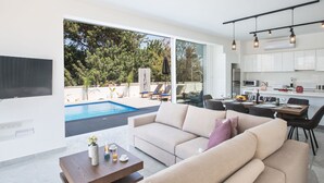 Ein modernes Wohnzimmer mit großem Fenster, Pool und Küchenbereich.