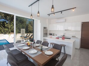 A modern dining area with a pool view, a kitchen with white cabinets, and a bar area. - 4-Schlafzimmer-Villa mit Pool im Zentrum von Protaras by Interhome (Protaras)
