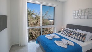 Ein Hotelzimmer mit großem Fenster, einem Bett mit blauer Bettwäsche und einer Wand mit gerahmten Bildern.