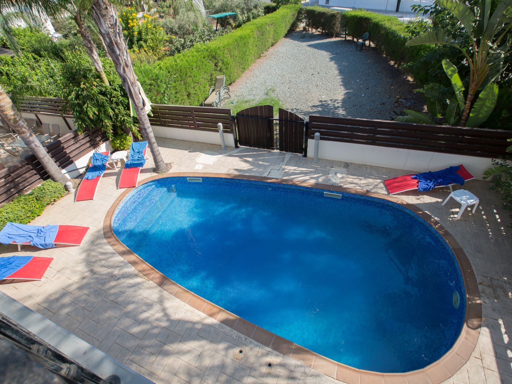 Een buitenzwembad met betegeld zonnedek, omringd door ligstoelen en een kleine tuin.