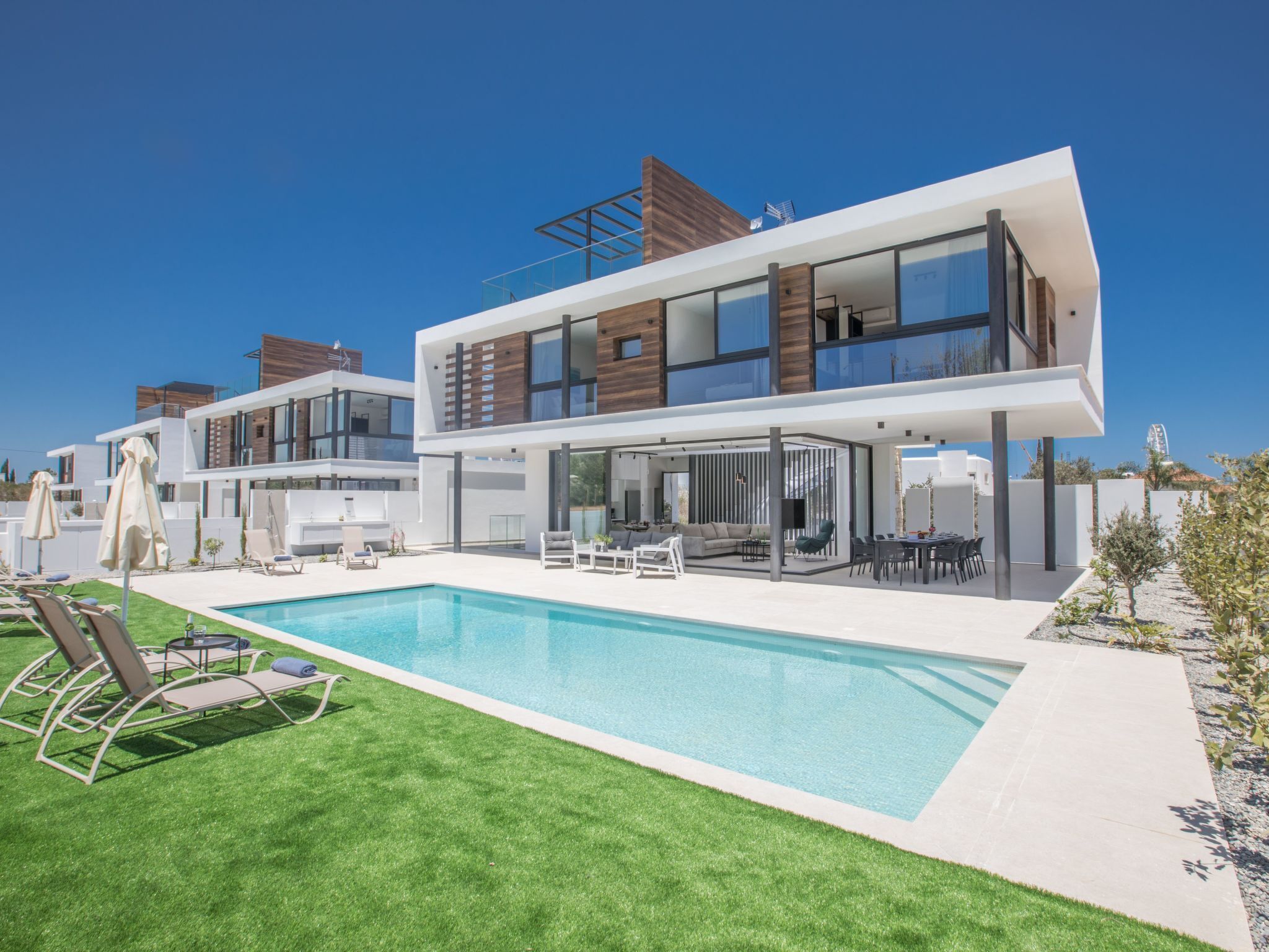 Ein modernes, zweistöckiges Haus mit Swimmingpool, Sitzgelegenheiten im Freien und freiem Blick zum Himmel.