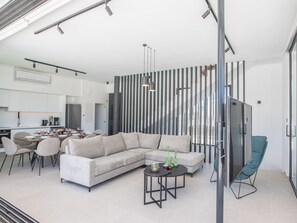 A modern living room with a sectional sofa, a dining area with chairs, and a kitchen in the background. - Geräumige Villa mit großem Garten und Pool by Interhome (Protaras)