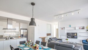 A modern kitchen with white cabinets, a stainless steel refrigerator, and a dining area with a table set for four. - Schöne Villa Olivine Pearl OL5 mit Garten by Interhome (Protaras)