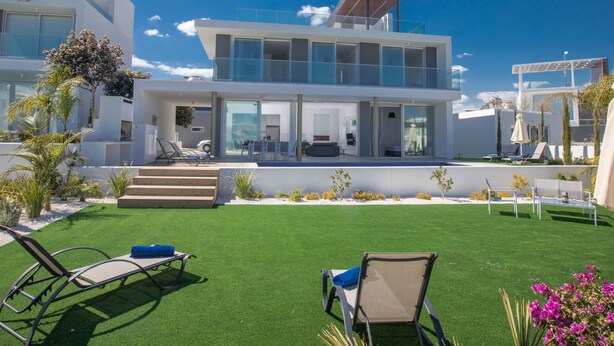 A modern two-story house with a flat roof, large glass windows, and a well-maintained lawn with artificial grass and outdoor furniture. - Schöne Villa Olivine Pearl OL5 mit Garten by Interhome (Protaras)